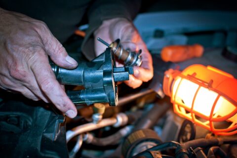 A man repairs a MINI Cooper engine, focusing on the faulty thermostat housing issue